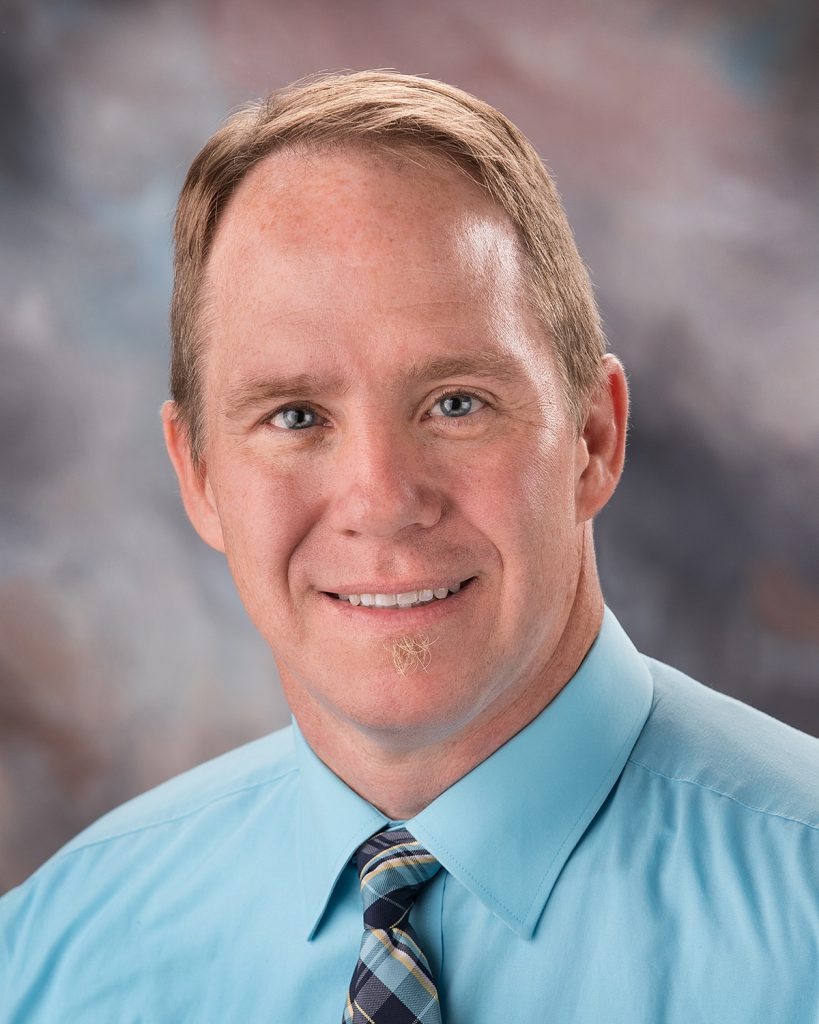 Headshot of Burke Kufeld, a white man in a blue collared shirt.